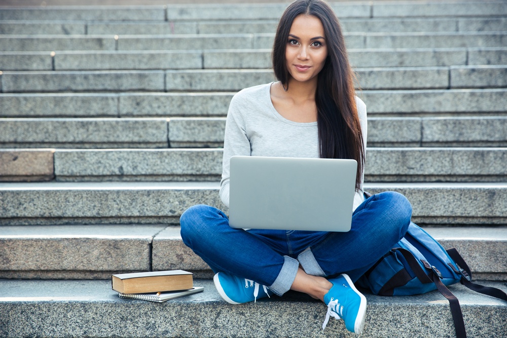 Portrait Of A Happy Young Woman Sitting On The City Stairs And Using Laptop Computer Outdoors